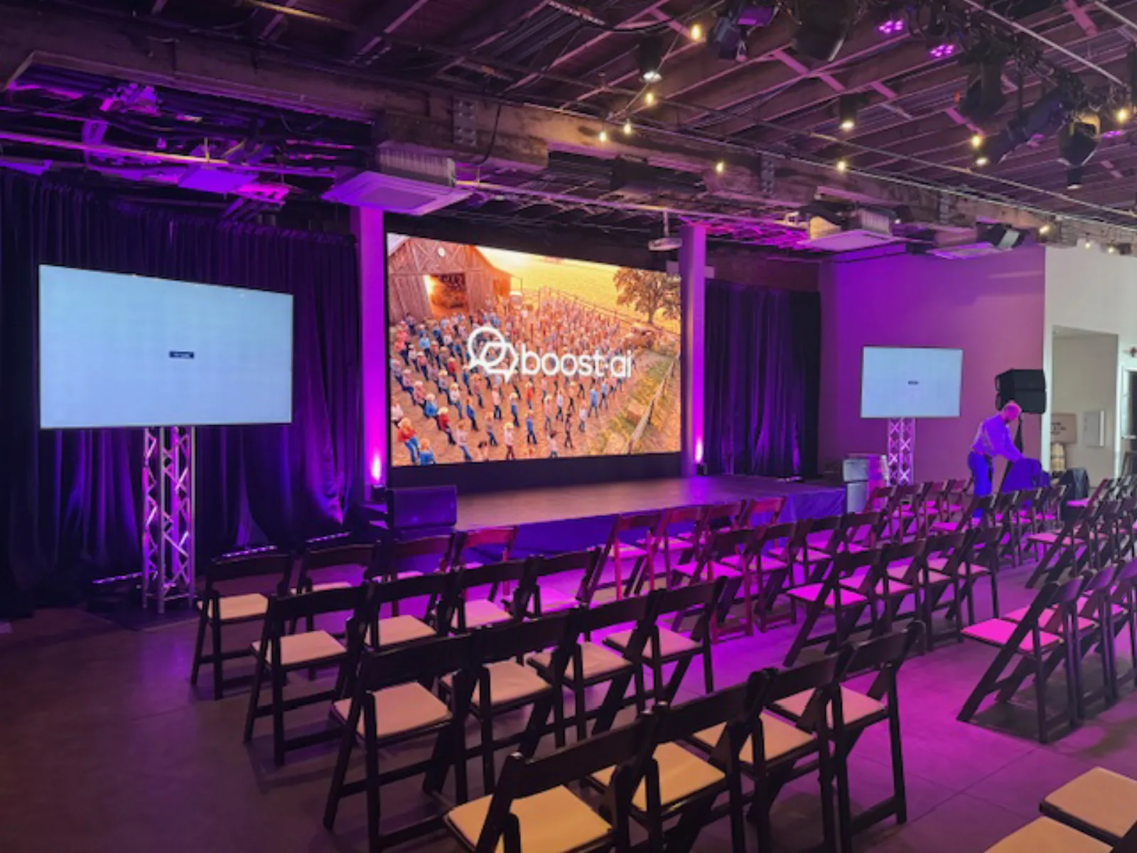 Corporate event stage at Acme Feed & Seed in downtown Nashville — large LED video wall flanked by dual 86-inch displays, purple uplighting and rows of folding chairs, produced by Nashville Audio Visual