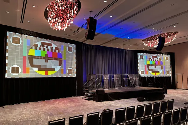 Draped stage with four clear acrylic lecterns between two large projection screens and flown line arrays in a Nashville ballroom