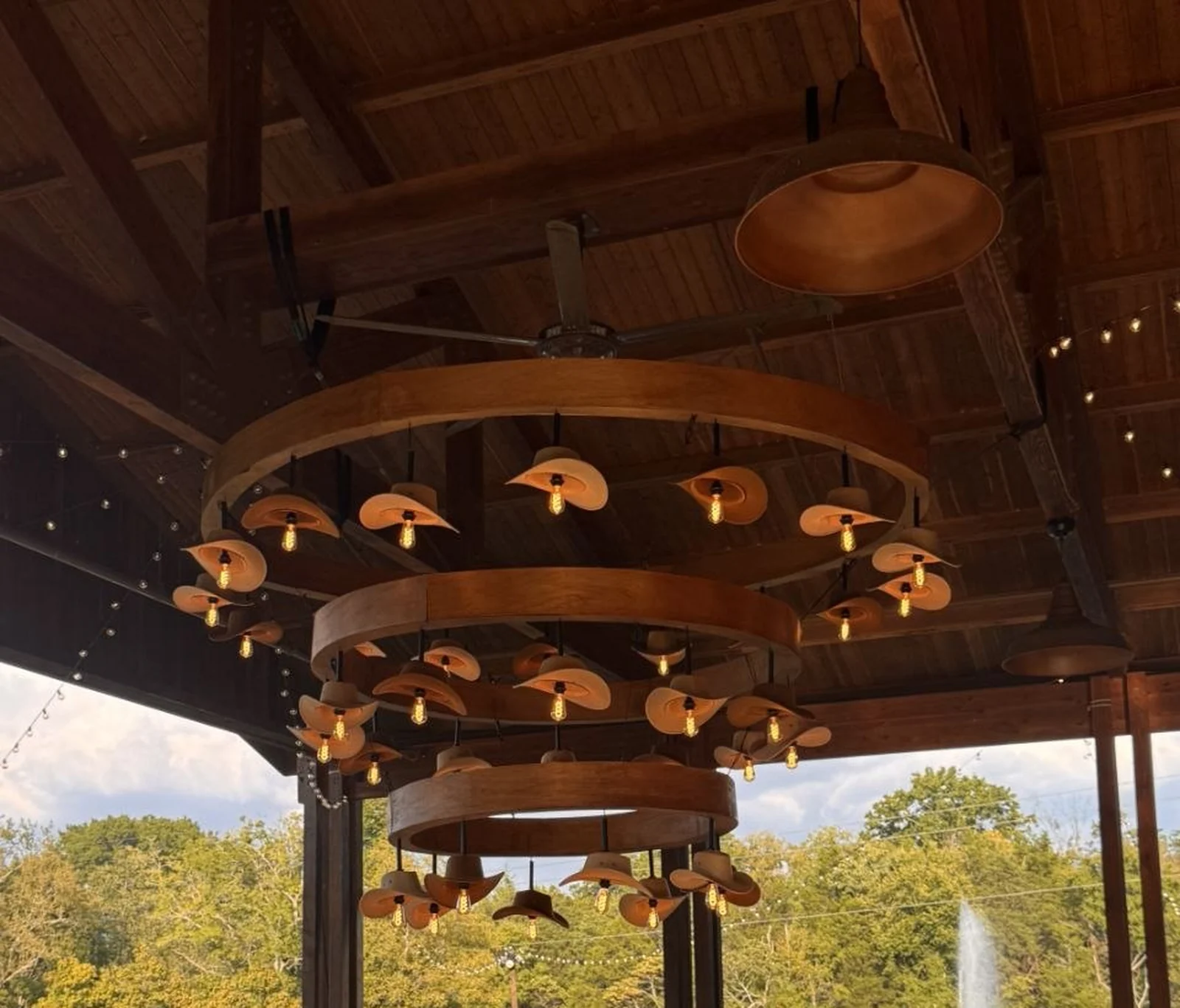 The custom cowboy hat chandelier built by Nashville Audio Visual — three tiered wooden rings, every cowboy hat fitted with its own Edison bulb, hanging over the green bar at The Barn at Sycamore Farms